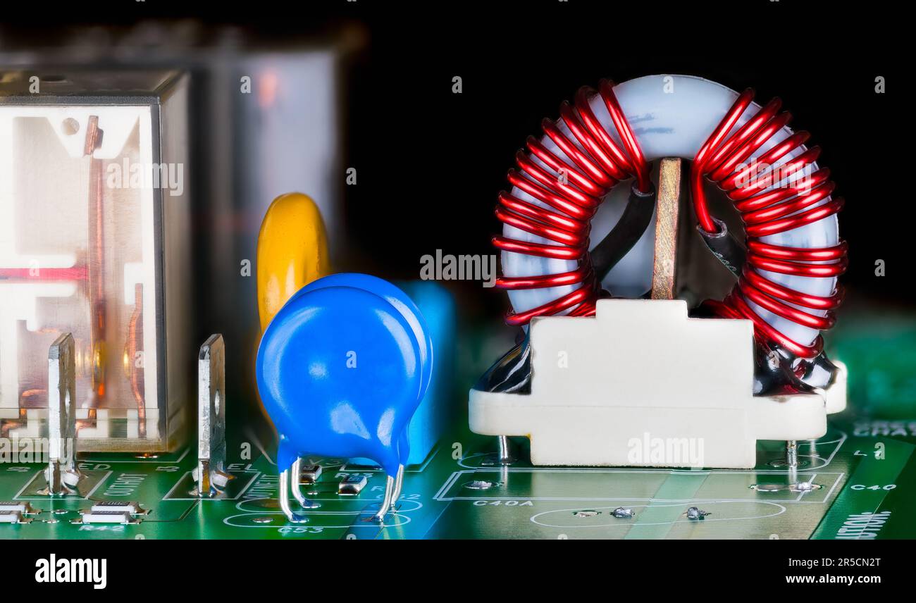 Gros plan sur une bobine à noyau toroïdal dans une carte de circuit imprimé électronique sur fond noir. Condensateur, résistance ou relais électromagnétique des composants électriques. Banque D'Images