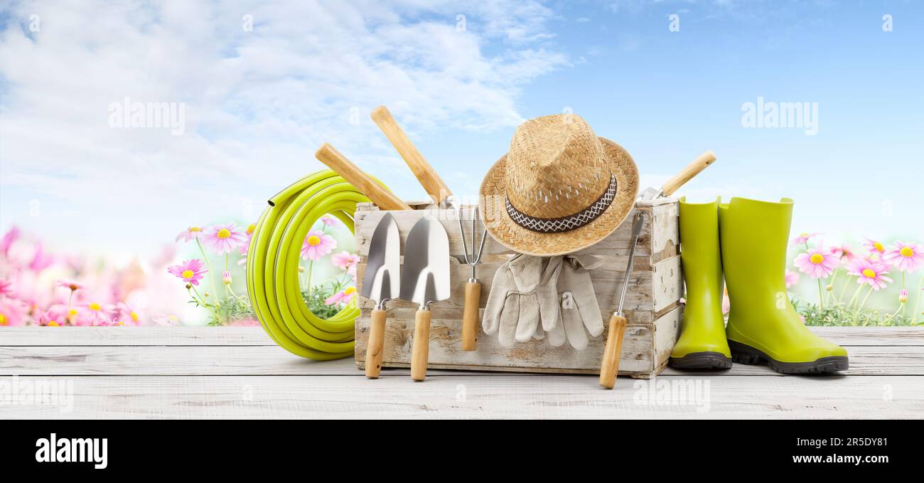 Équipement d'outils de jardinage, caisse en bois avec kit de jardin, bottes en caoutchouc vert, tuyau, truelle de poignée et chapeau de paille sur table en bois blanc avec fleur et sk Banque D'Images