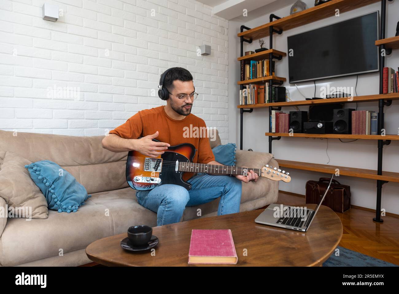 Jeune musicien débutant, débutant, portant un casque moderne, apprenant à jouer de la guitare et à enregistrer de la musique lors d'un cours de vidéo sur le Web à l'aide d'un ordinateur portable. Concentré millénaire Banque D'Images