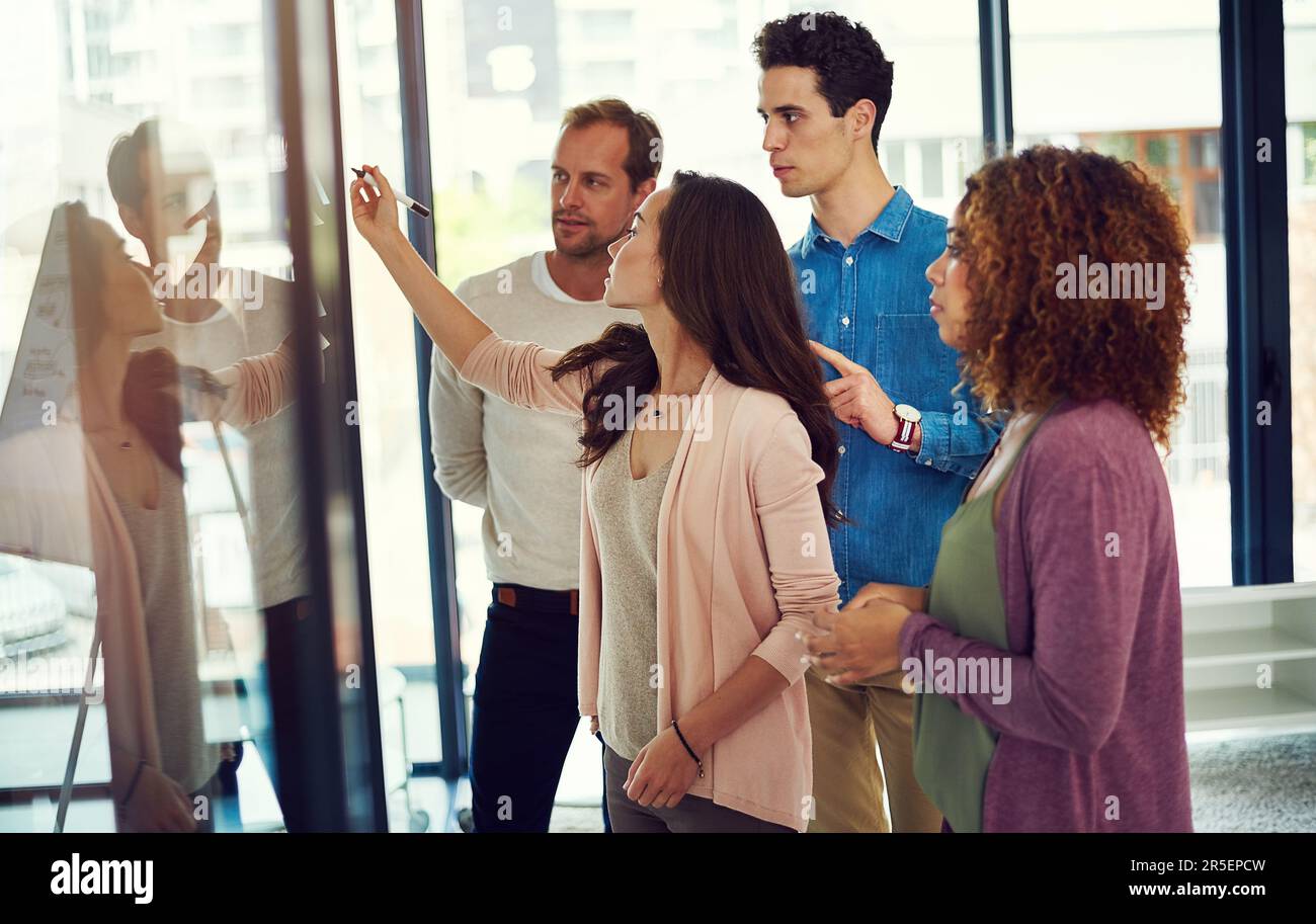 Associer leur expertise pour obtenir de grands résultats. un groupe de jeunes designers remue-méninges avec des notes sur un mur de verre dans un bureau. Banque D'Images