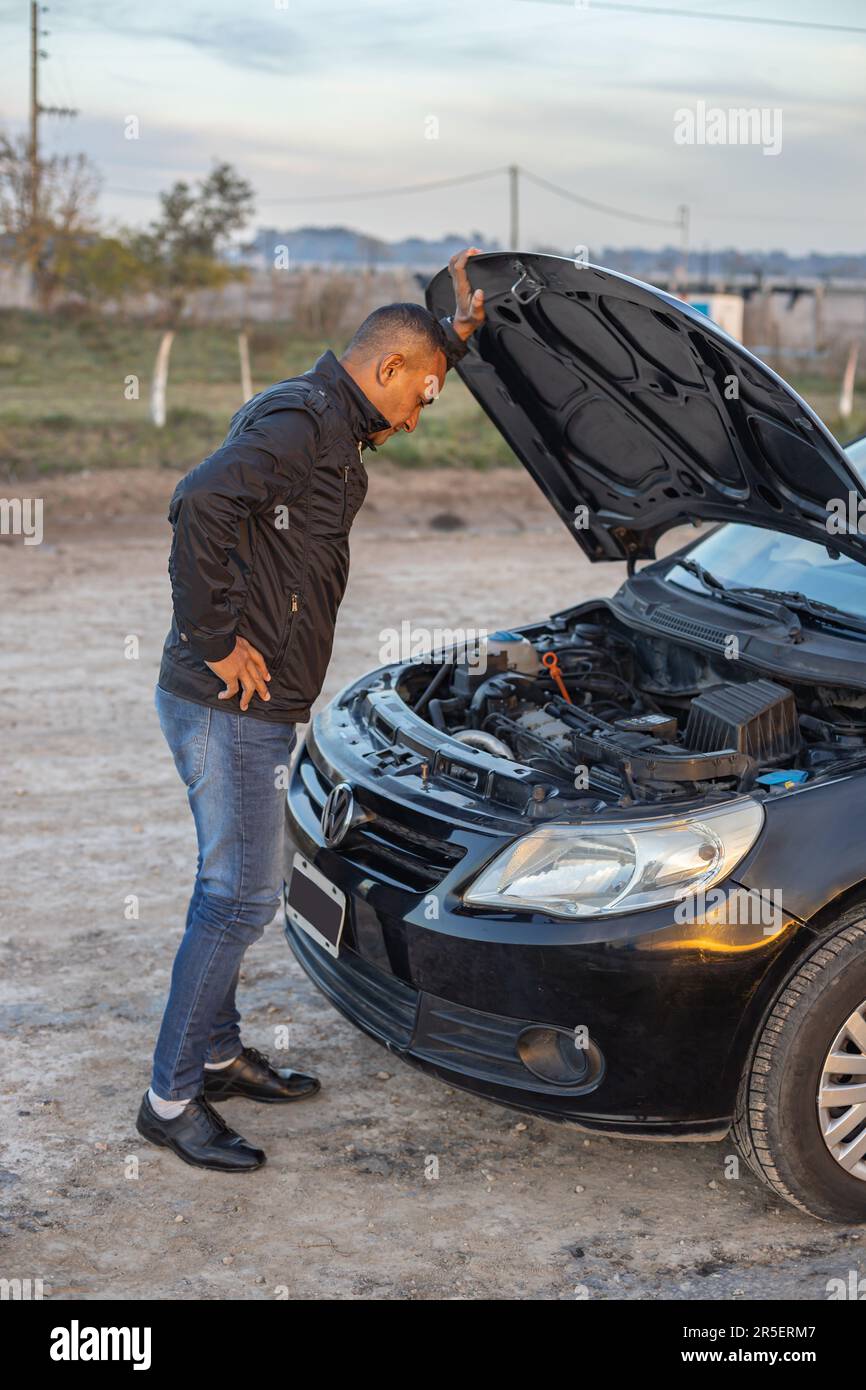 Jeune Latino homme regardant le moteur de sa voiture en panne sur le côté de la route. Banque D'Images