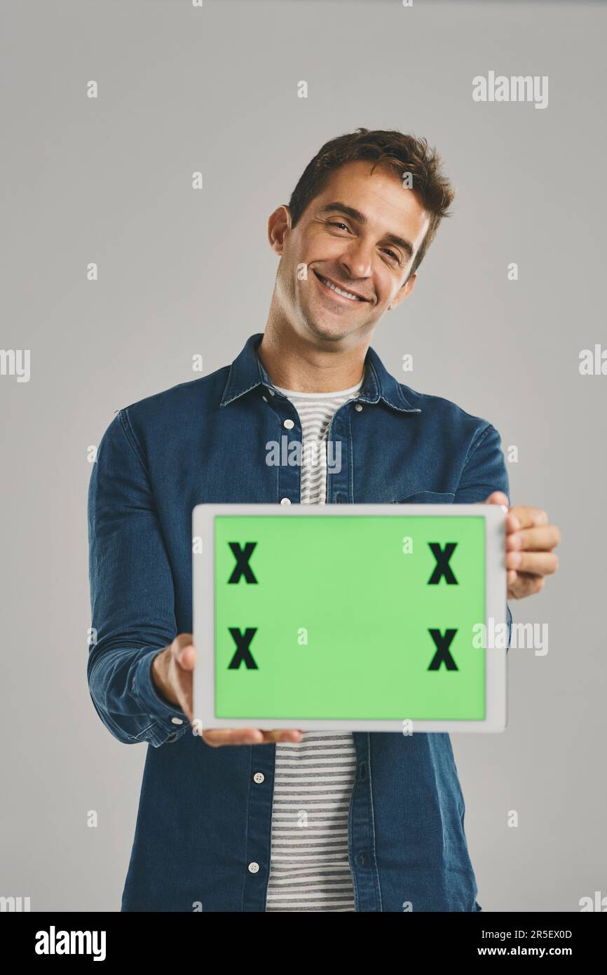 C'est le site que je visite tous les jours. Portrait studio d'un jeune homme tenant une tablette numérique avec un écran vert sur fond gris. Banque D'Images