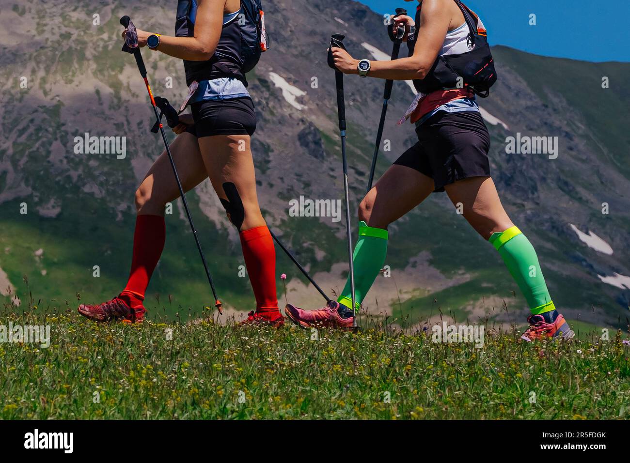 deux femmes sentier de marche sur prairie verte en arrière-plan montagne, chaussettes de compression sur ses pieds et bâtons de randonnée dans les mains Banque D'Images
