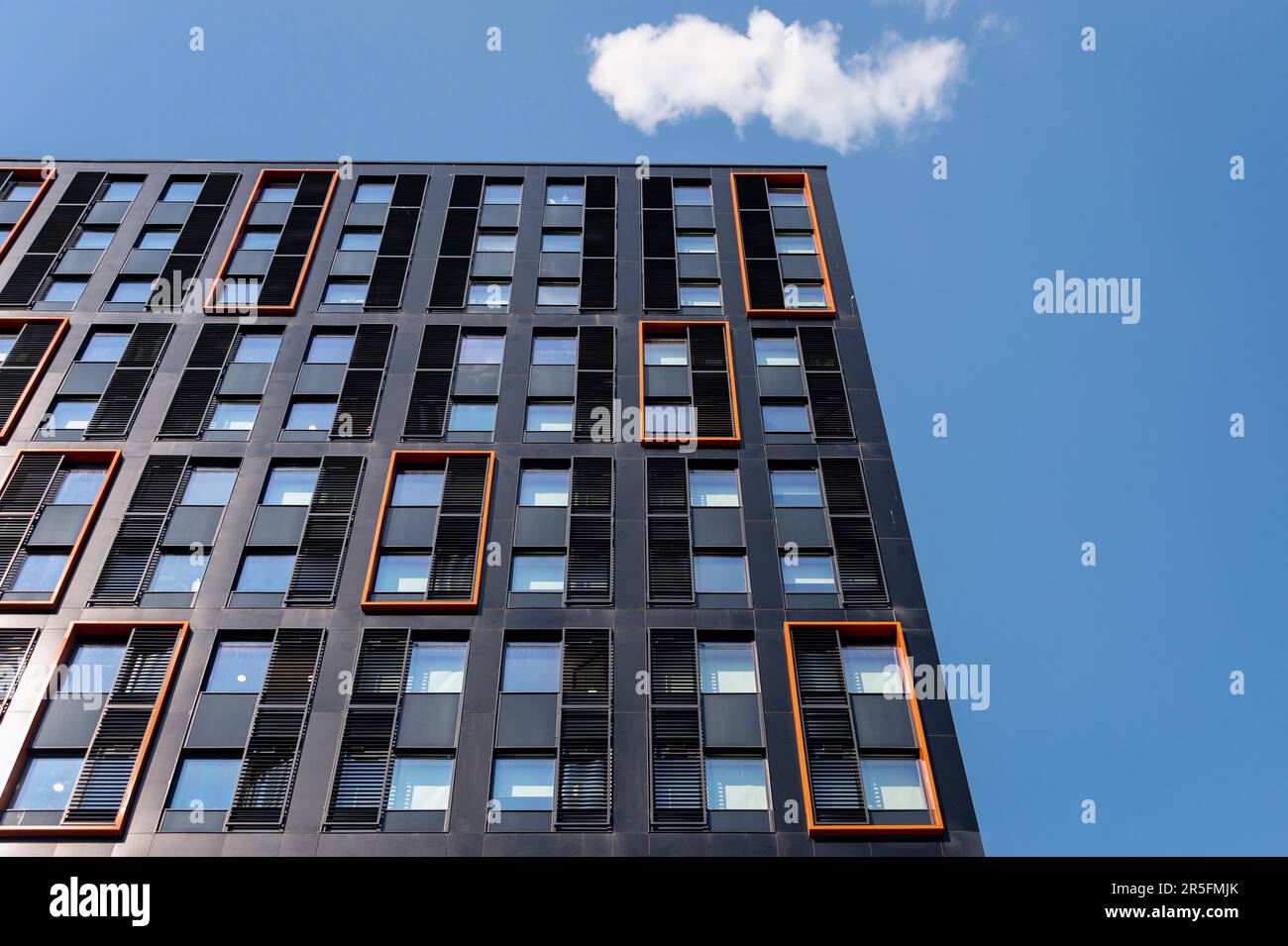 Bâtiment moderne noir et orange face à un ciel bleu, en regardant vers le haut. Banque D'Images