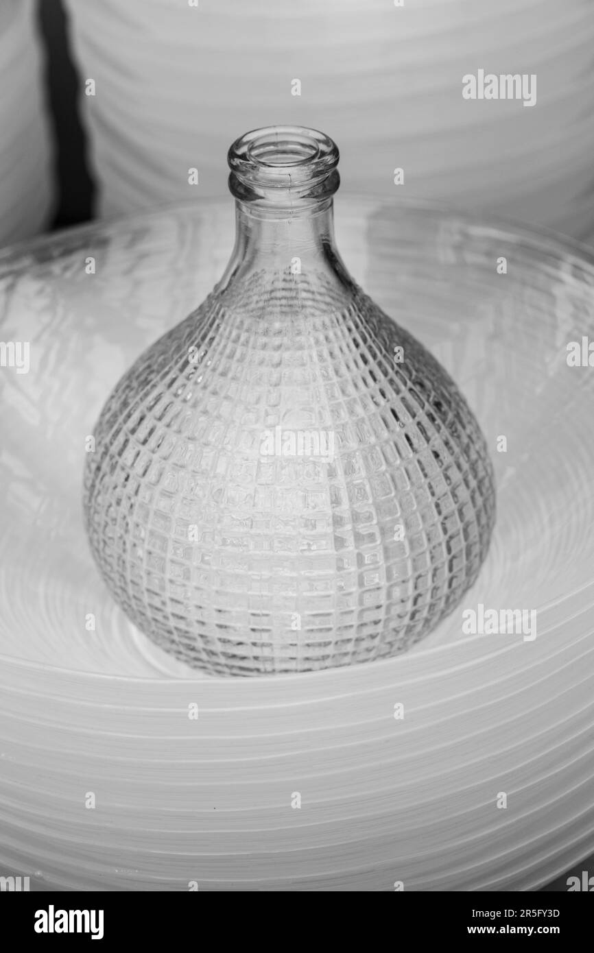 Une bouteille en verre bulbeuse repose sur une pile de plaques. Banque D'Images