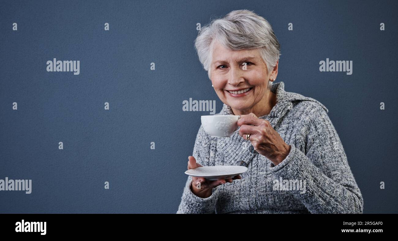 C'est une bonne tasse de thé. Photo en studio d'une femme âgée gaie assise et prenant une tasse de thé tout en regardant l'appareil photo. Banque D'Images