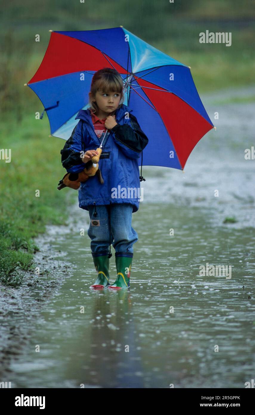 Fille avec parapluie et bottes en caoutchouc tient dans énorme pluie flaque Banque D'Images