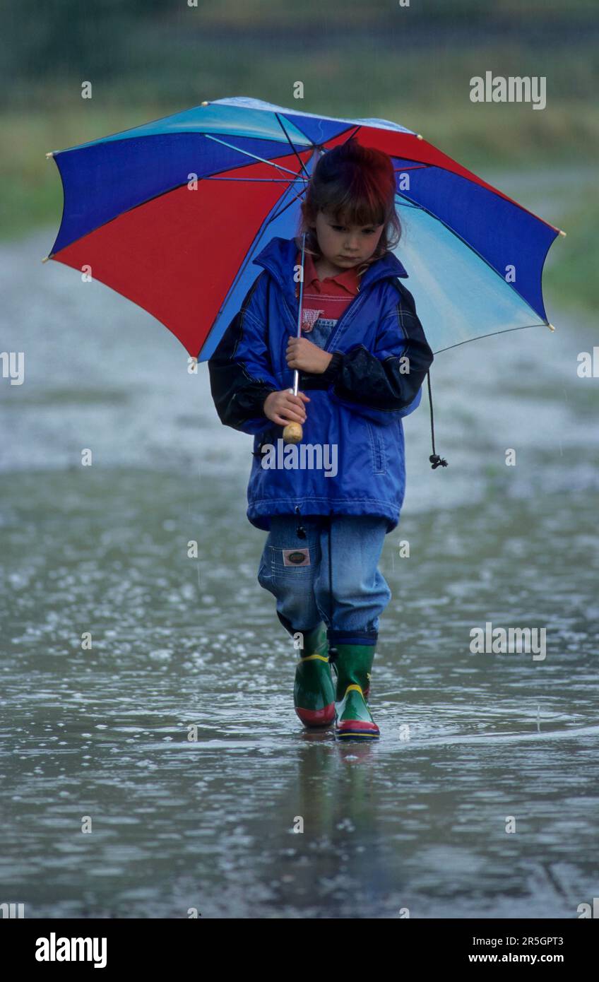 Fille avec parapluie et bottes en caoutchouc tient dans énorme pluie flaque Banque D'Images