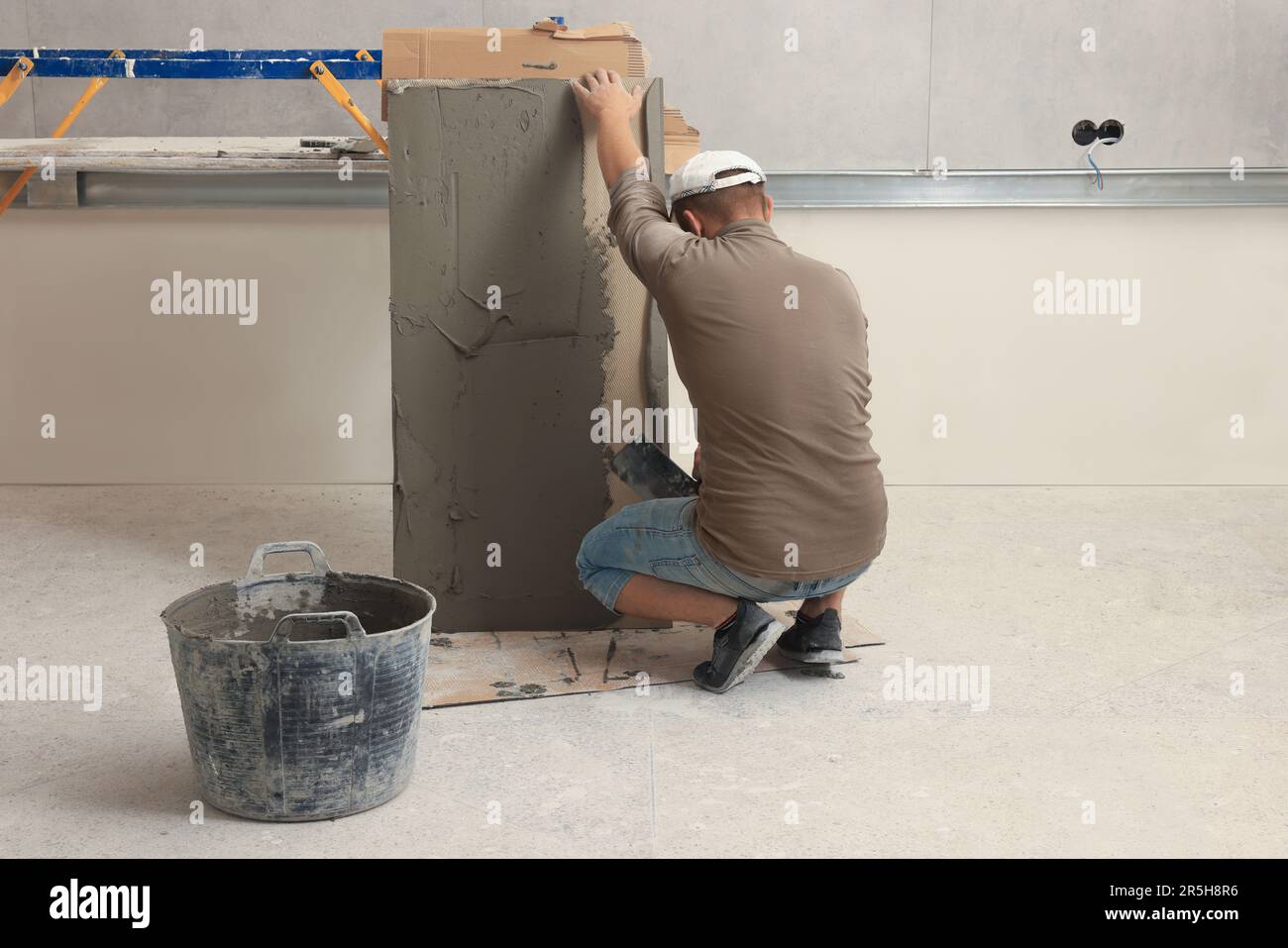 Le travailleur répartissant le mélange d'adhésif sur les carreaux avec une spatule Banque D'Images