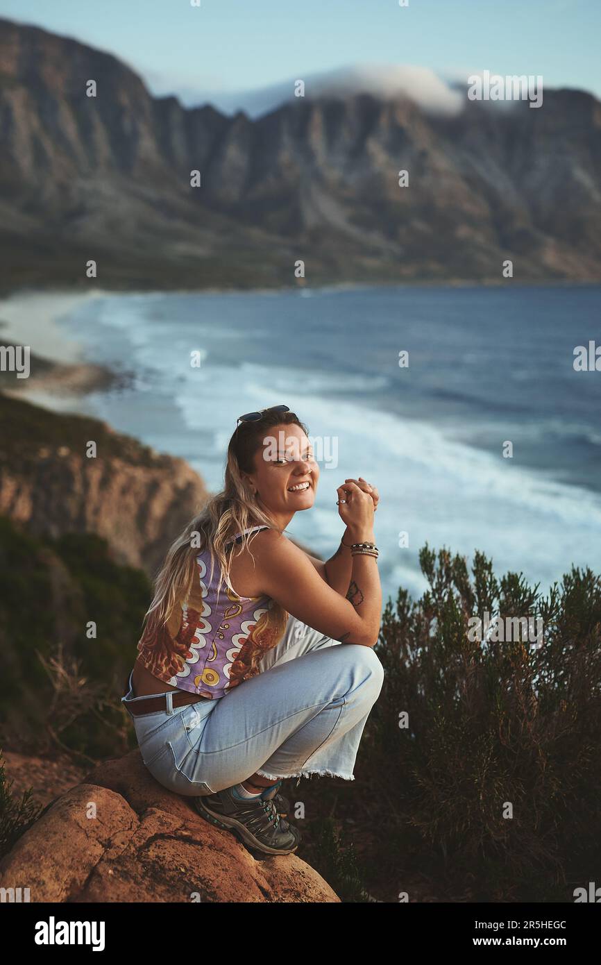 Je ne manque pas ce coucher de soleil. Portrait en longueur d'une jeune femme attirante s'est enroulée sur le flanc de la montagne, près de la mer seule pendant une journée à l'extérieur. Banque D'Images