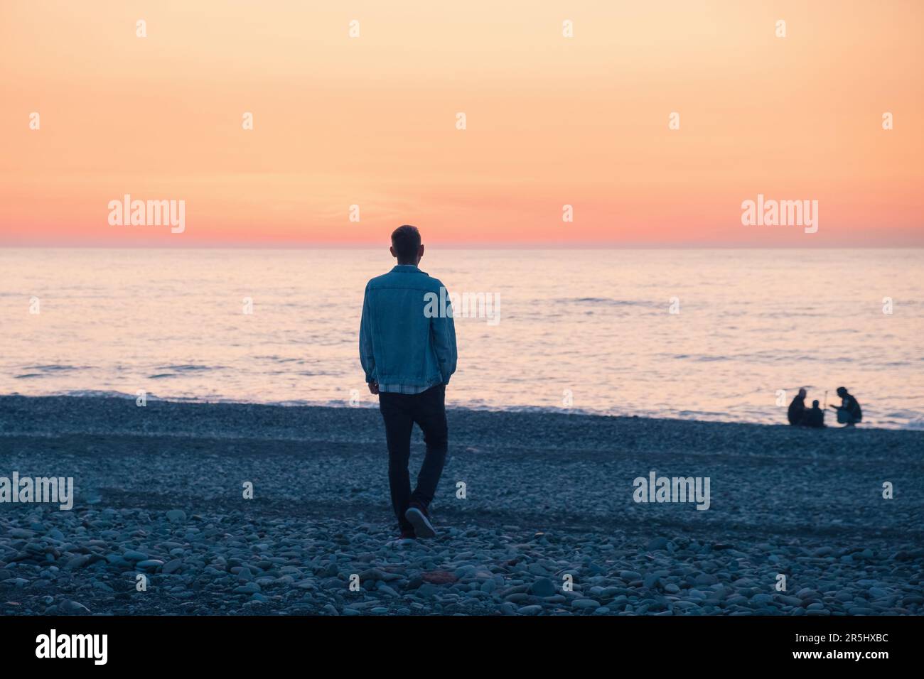 Homme solitaire marchant sur la côte de la mer au coucher du soleil. Homme avec des problèmes mentaux sur la plage au bord de l'océan. Solitude, dépression, mélancolie, stress Banque D'Images