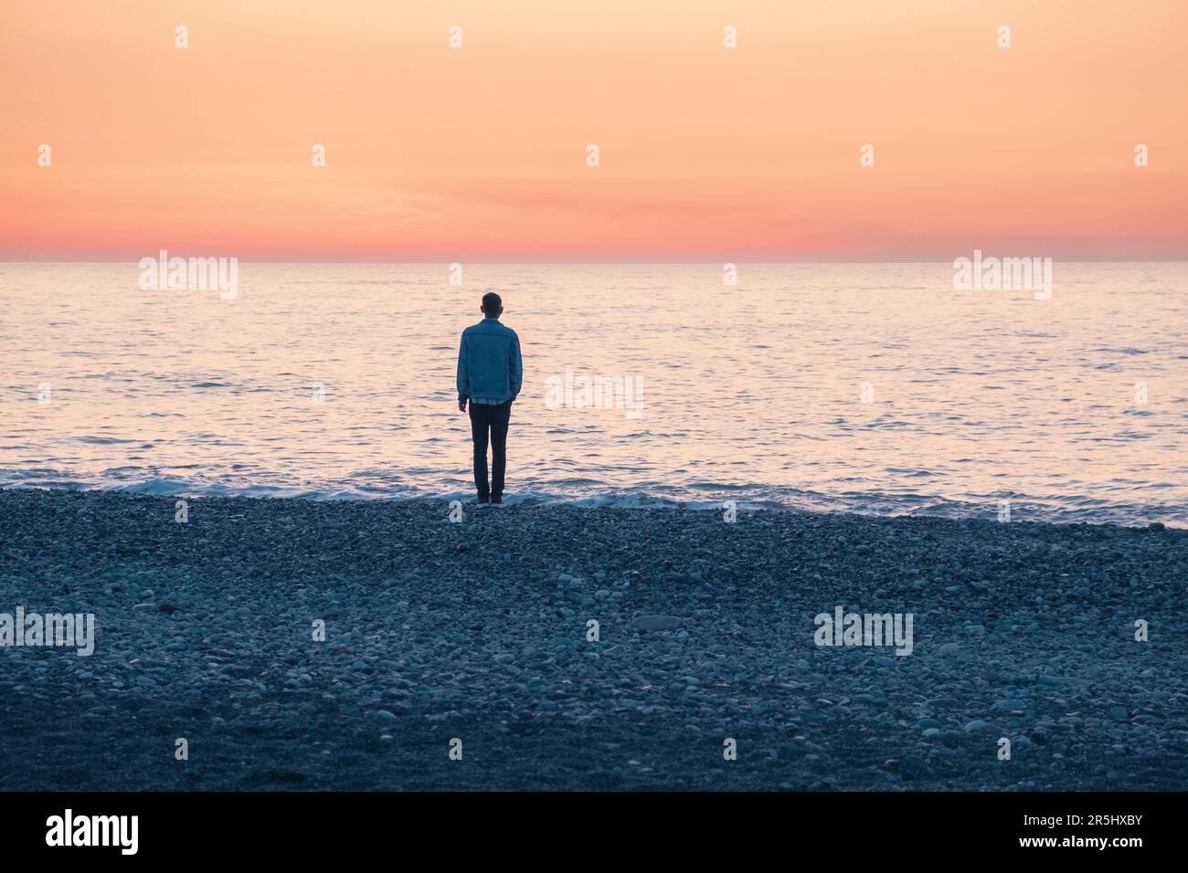 Homme solitaire debout sur la côte de la mer au coucher du soleil. Homme avec des problèmes mentaux sur la plage au bord de l'océan. Solitude, dépression, mélancolie, stress Banque D'Images