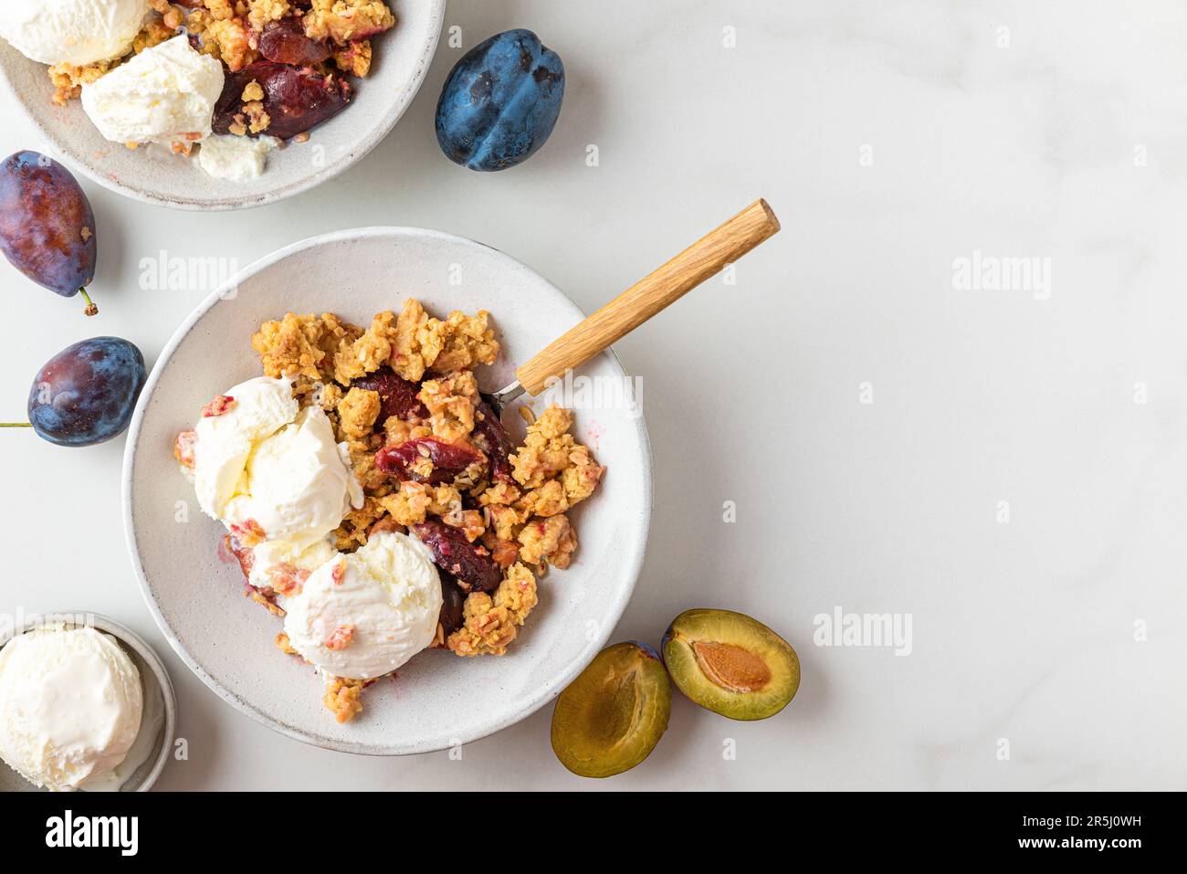 Crumble aux prunes avec glace à la vanille sur fond blanc. Dessert aux fruits croustillants de l'été. Vue de dessus avec espace de copie Banque D'Images