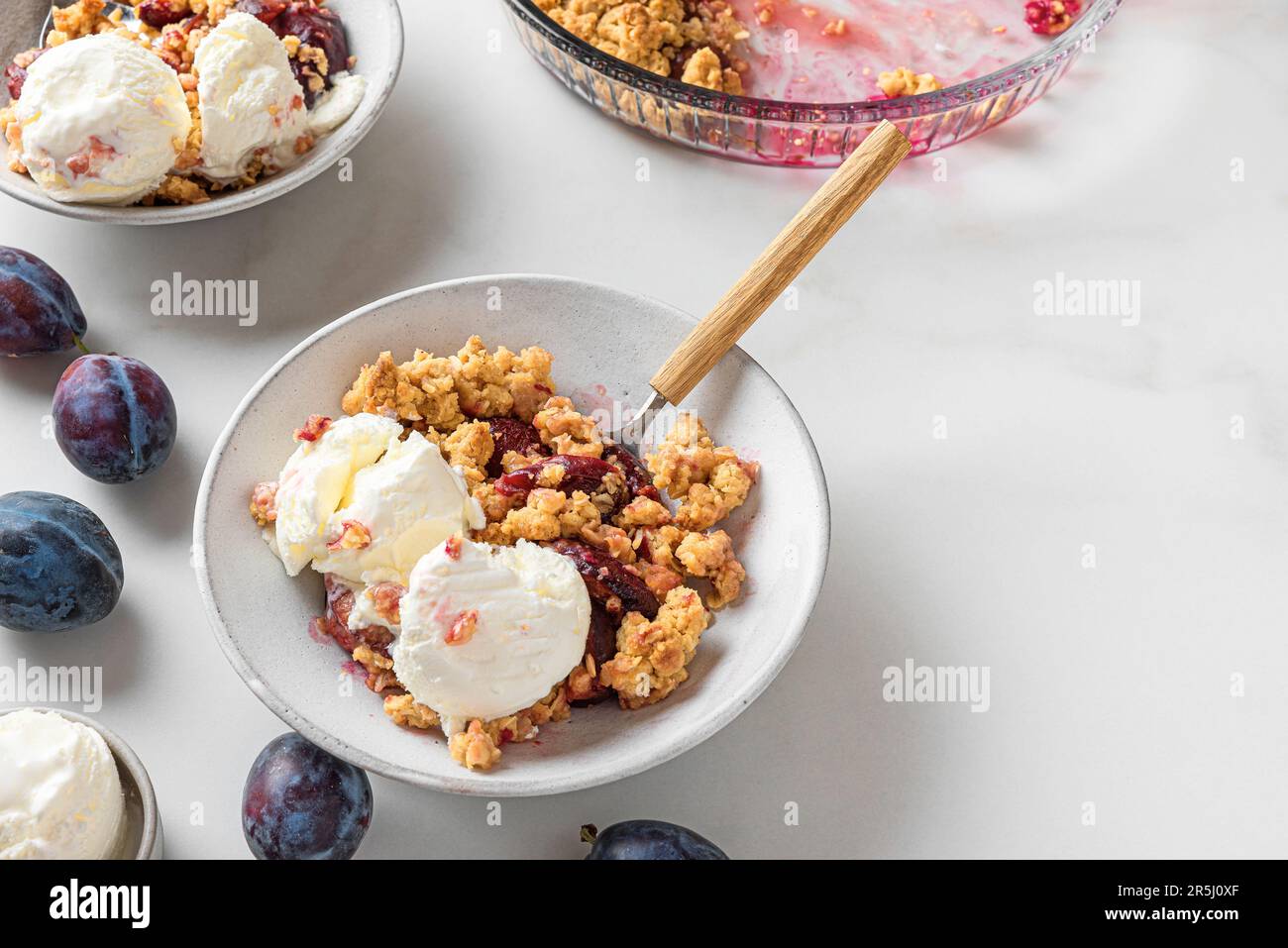 Crumble aux fruits. Tarte aux prunes avec glace à la vanille dans des assiettes avec des cuillères sur une table en marbre blanc Banque D'Images