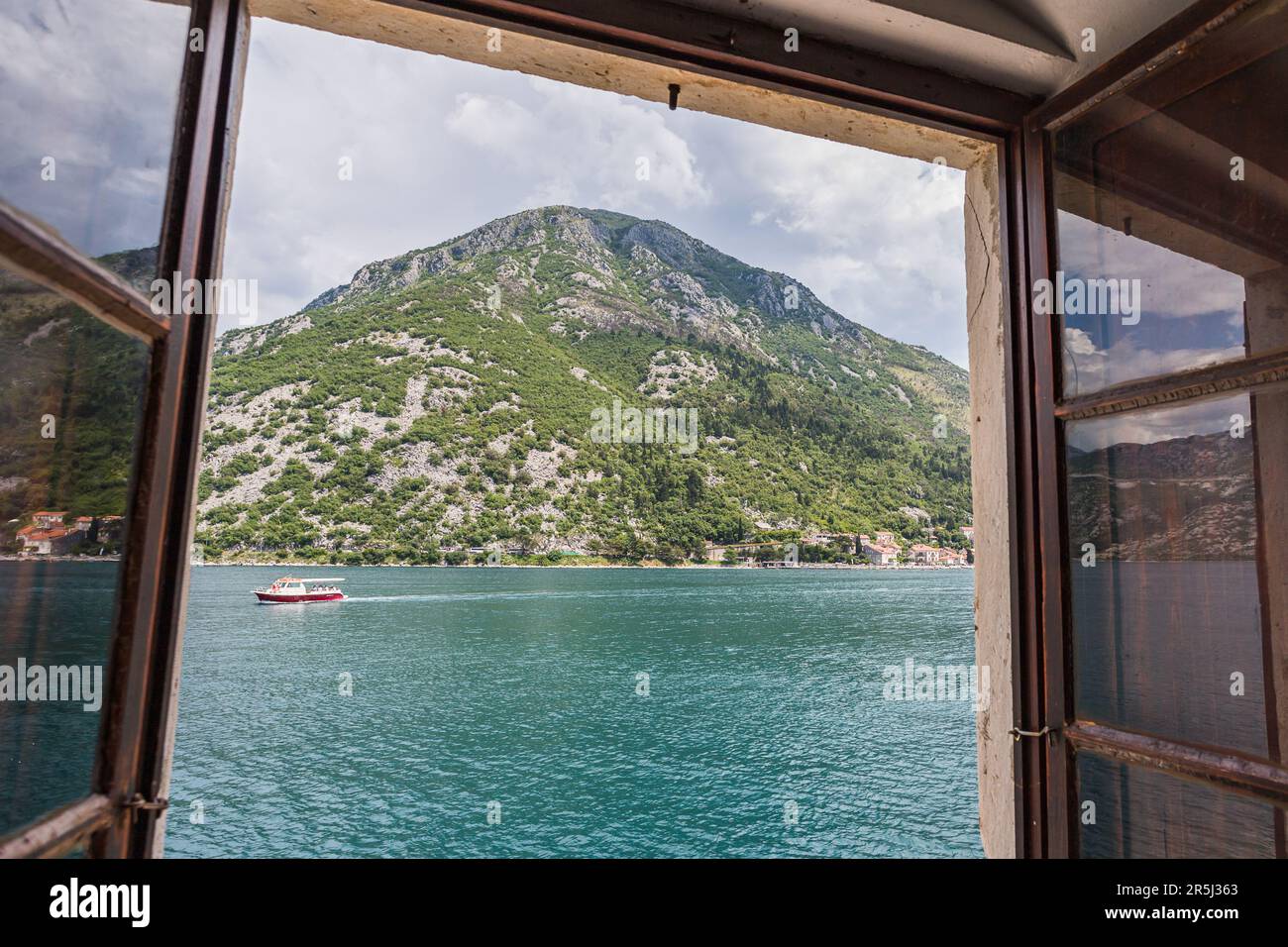 Un bateau vu voyageant le long de la baie de Kotor au pied d'une montagne, pictued de notre Dame des rochers en mai 2023. Banque D'Images