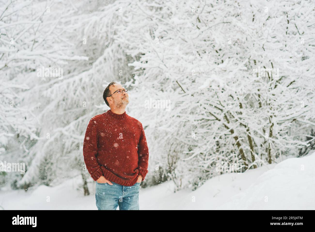 Portrait extérieur de l'âge moyen 55 - 60 ans homme appréciant le beau temps froid dans la forêt d'hiver, portant le pull-over rouge tricoté Banque D'Images