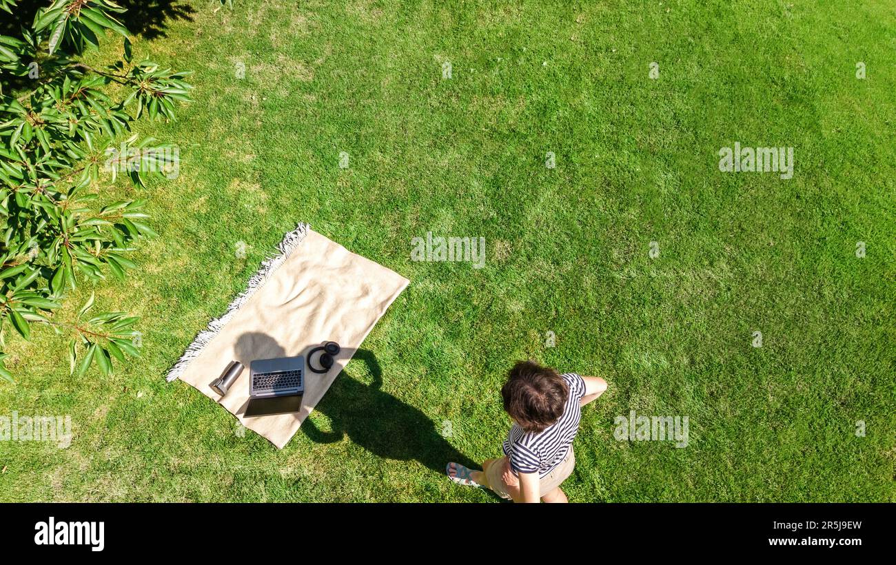 Jeune femme avec ordinateur portable dans le parc, étudiante fille freelance travaillant et étudiant en ligne à l'extérieur sur l'herbe avec des écouteurs et ordinateur portable Banque D'Images