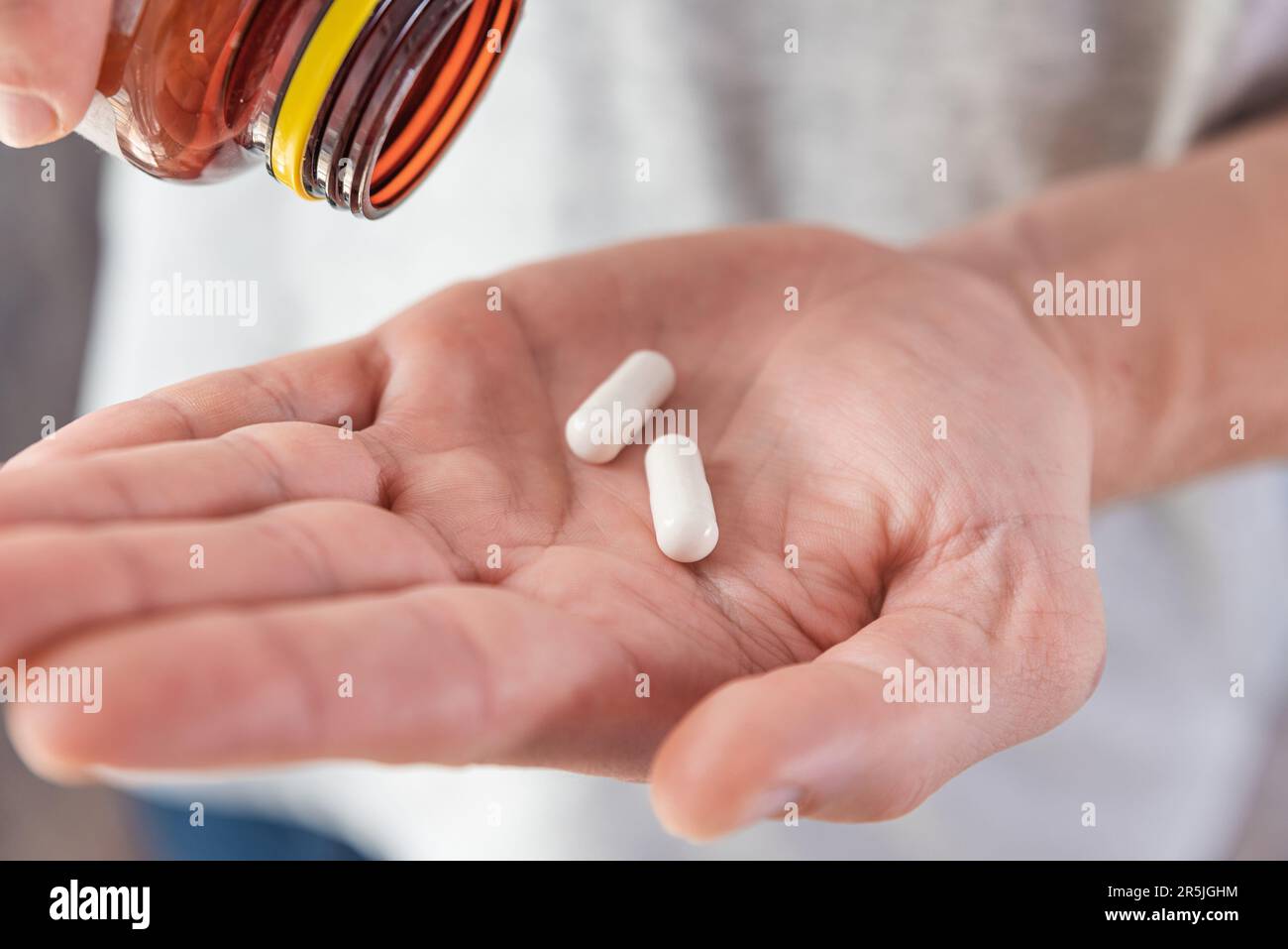 Homme versant des capsules blanches avec du collagène dans la main mâle à partir d'une bouteille de médicament. Supplément nutritionnel, médicaments, médicaments pour la protection des articulations, soins de la peau Banque D'Images