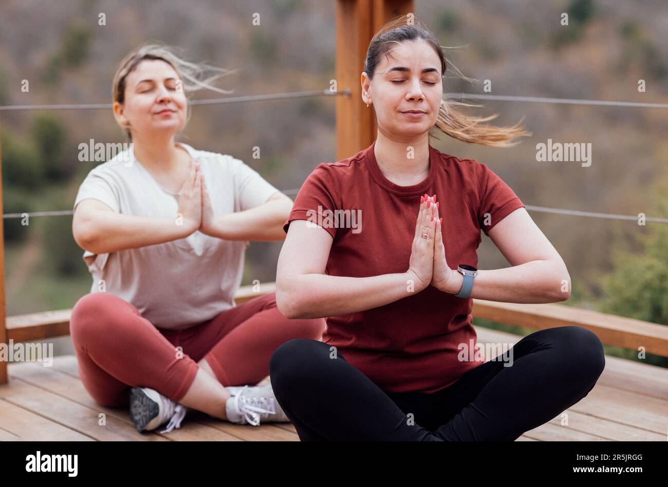 Deux jeunes femmes s'entraîner à l'asana yoga dans le parc. Les filles souriantes sont assises en position lotus. Les amies méditent sur une plate-forme en bois à ciel ouvert. En bonne santé Banque D'Images