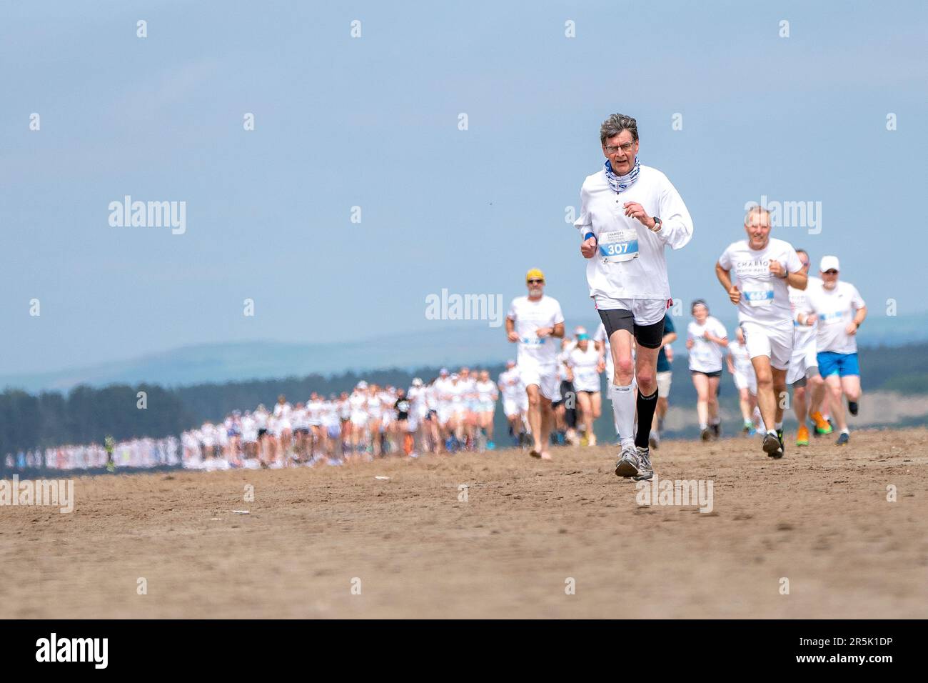 Les coureurs, qui portent du blanc, participent à la course annuelle des chars de feu le long de la plage de West Sands à St Andrews, Fife. La course de 5km participe au même endroit que la célèbre scène de course du film Chariots of Fire de 1981 a été filmée. Les recettes de l'événement sont remises au RNLI et aux organismes de bienfaisance locaux. Date de la photo: Dimanche 4 juin 2023. Banque D'Images