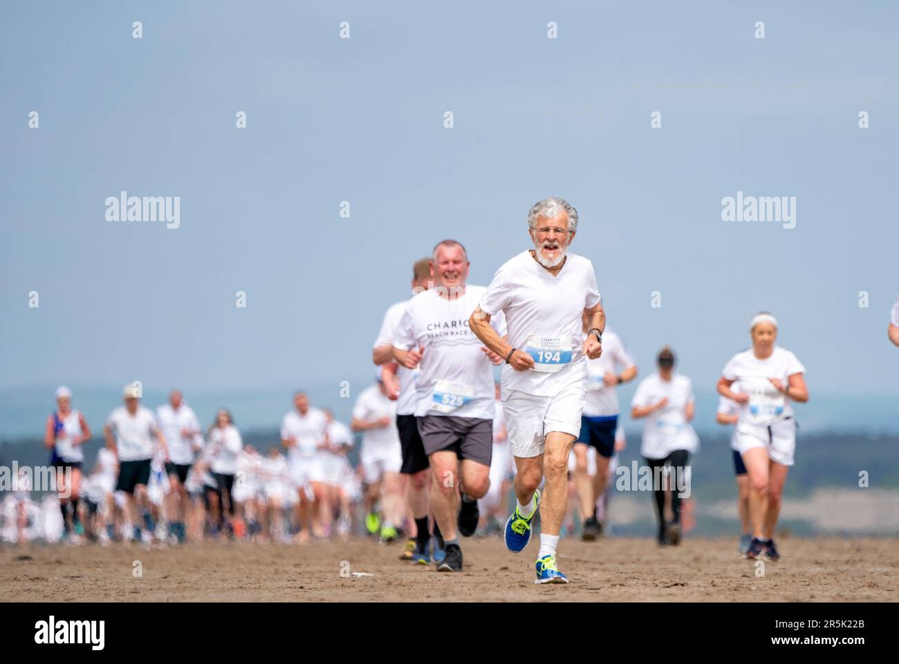 Les coureurs, qui portent du blanc, participent à la course annuelle des chars de feu le long de la plage de West Sands à St Andrews, Fife. La course de 5km participe au même endroit que la célèbre scène de course du film Chariots of Fire de 1981 a été filmée. Les recettes de l'événement sont remises au RNLI et aux organismes de bienfaisance locaux. Date de la photo: Dimanche 4 juin 2023. Banque D'Images