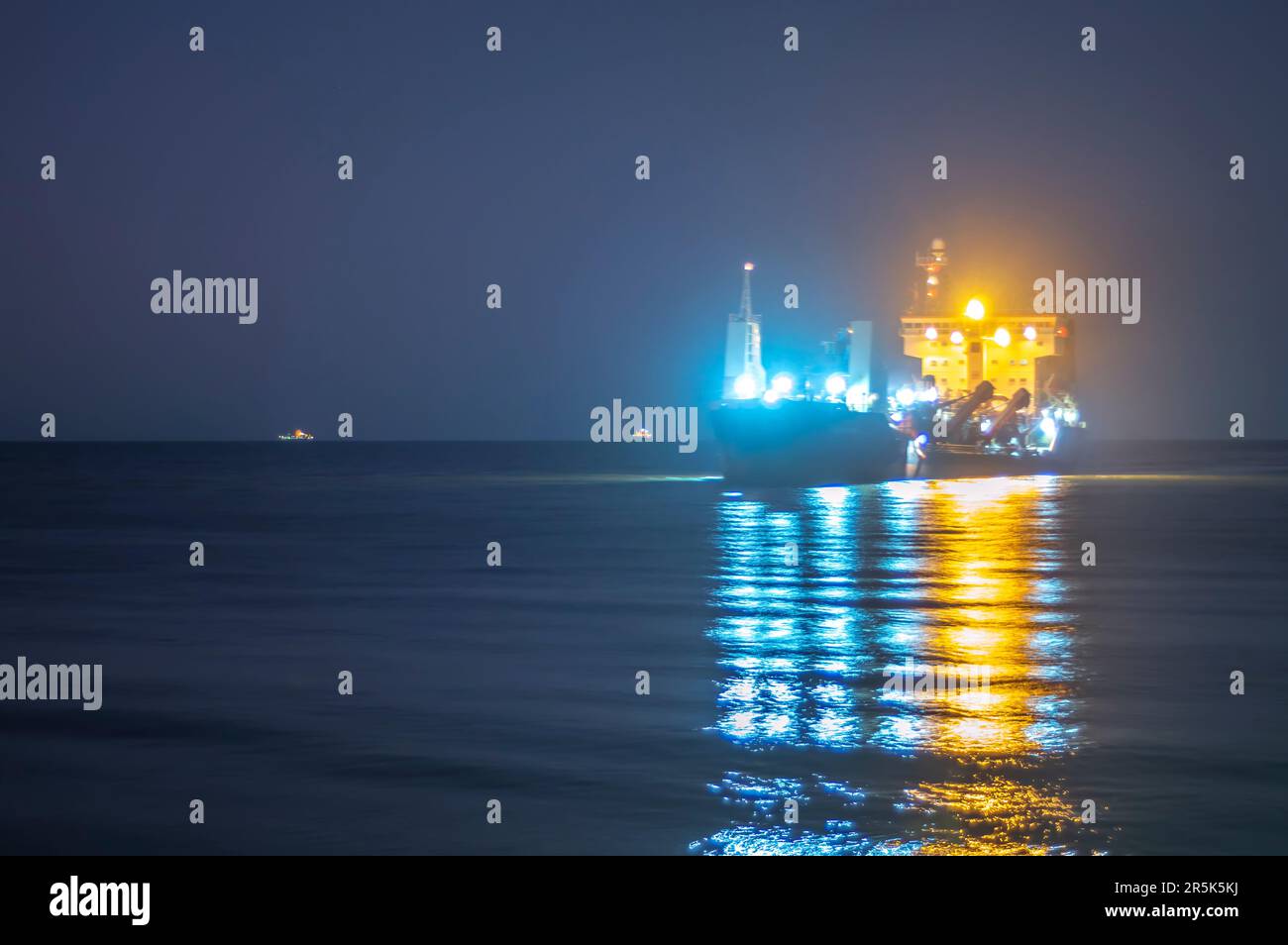 Bateau de cargaison naviguant en mer la nuit avec les lumières allumées, photo sur une longue exposition. Banque D'Images