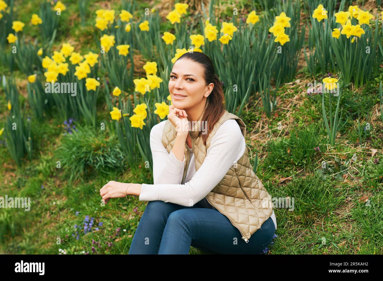 Portrait de printemps de la jeune belle femme assise dans un champ de jonquilles en fleurs Banque D'Images