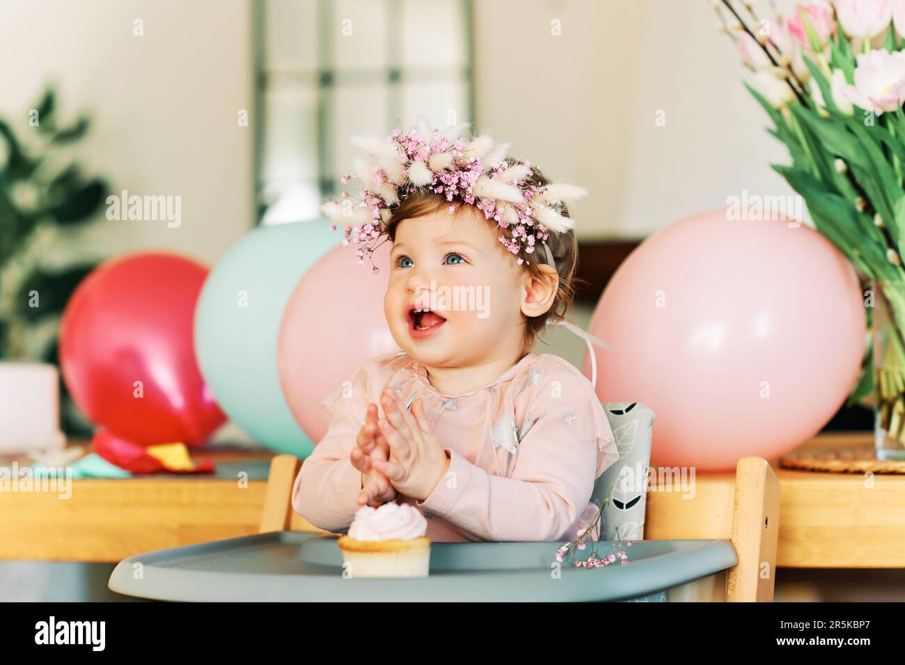 Adorable bébé fille de 1 ans mangeant un cupcake, enfant heureux assis dans une chaise, dégustation de dessert sucré, premier anniversaire Banque D'Images