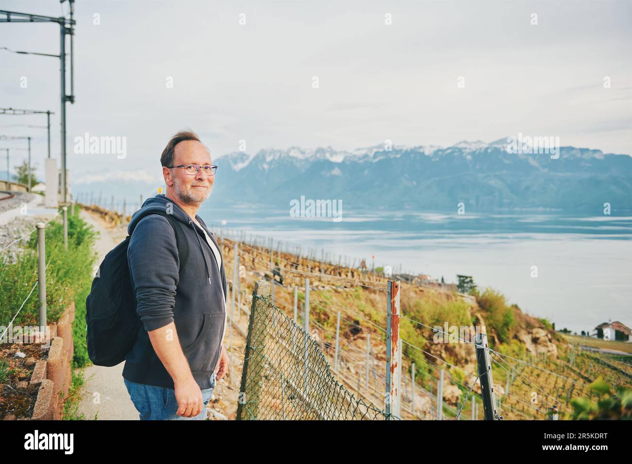 Homme d'âge moyen randonnée avec sac à dos, posant à côté des chemins de fer avec vue sur le lac de Genève et la haute-Savoie, Lavaux, Suisse Banque D'Images