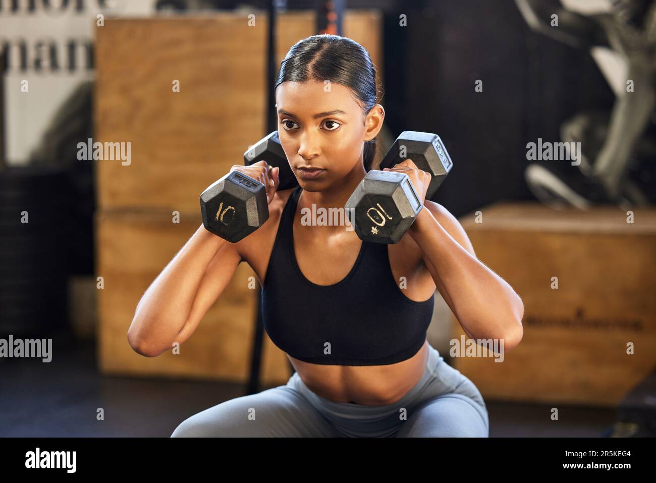 Fitness, squat ou femme avec haltères entraînement, exercice ou entraînement pour les bras ou les muscles puissants dans la salle de gym. Dumbbell squats, bodybuilder ou fille indienne Banque D'Images