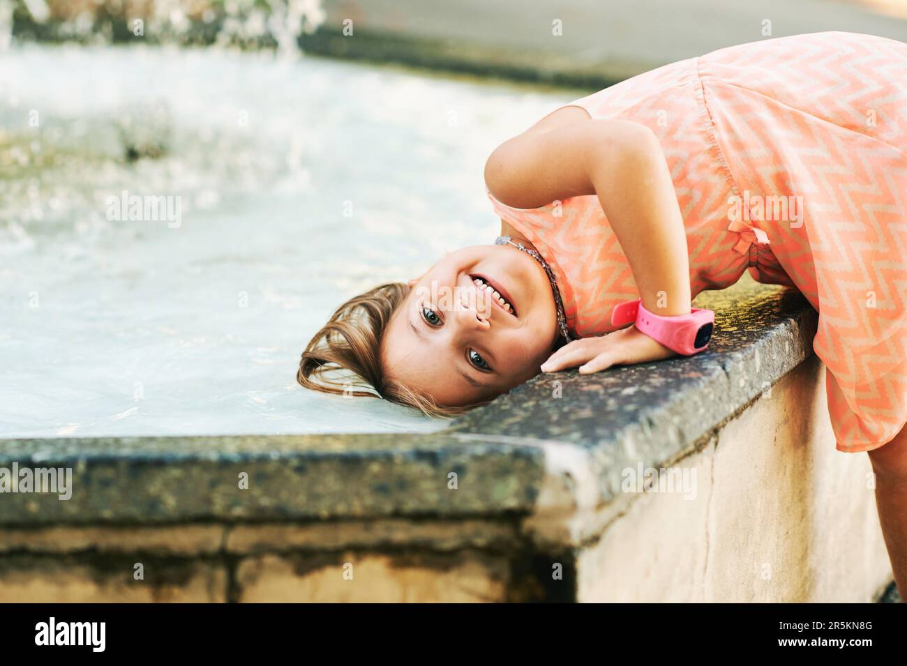 Drôle petite fille mouillant les cheveux dans la fontaine, chaud jour d'été, enfant jouant dehors Banque D'Images