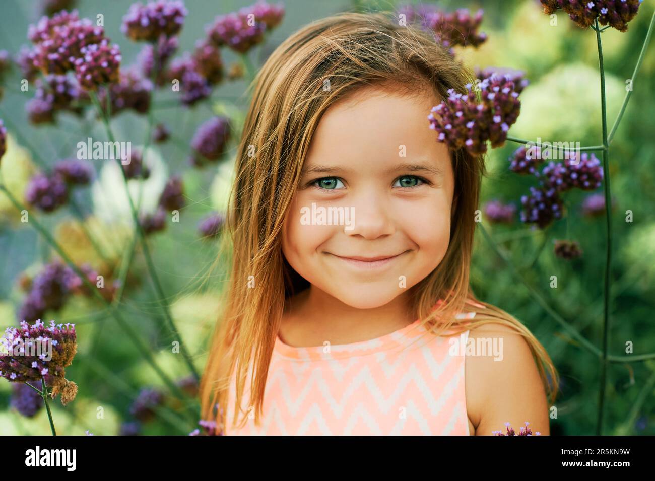 Portrait d'été extérieur d'une adorable petite fille de 3 ou 4 ans, posant dans des fleurs violettes Banque D'Images