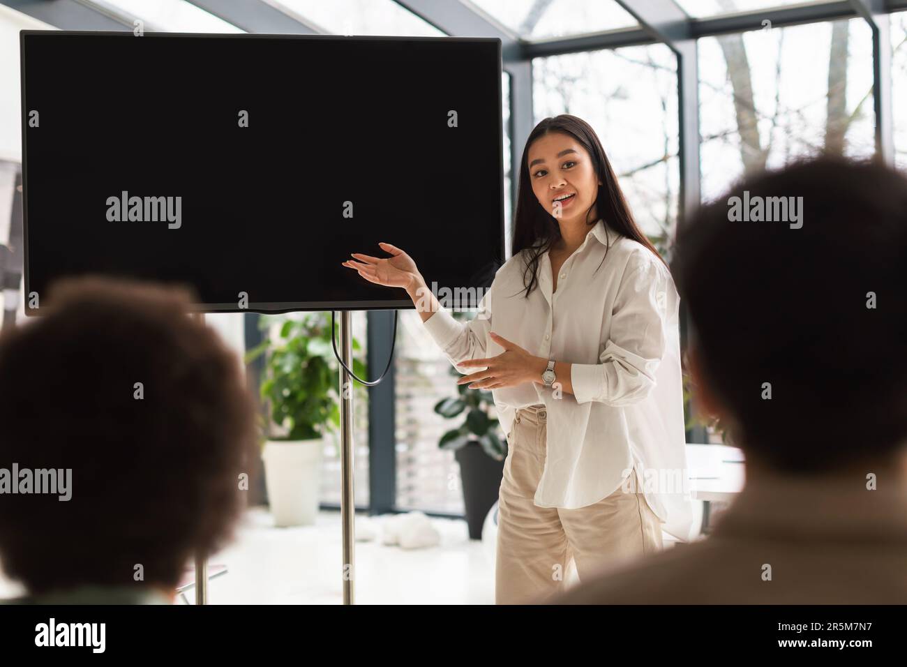 Une femme d'affaires japonaise qui donne un discours pointant vers l'écran dans le bureau moderne Banque D'Images