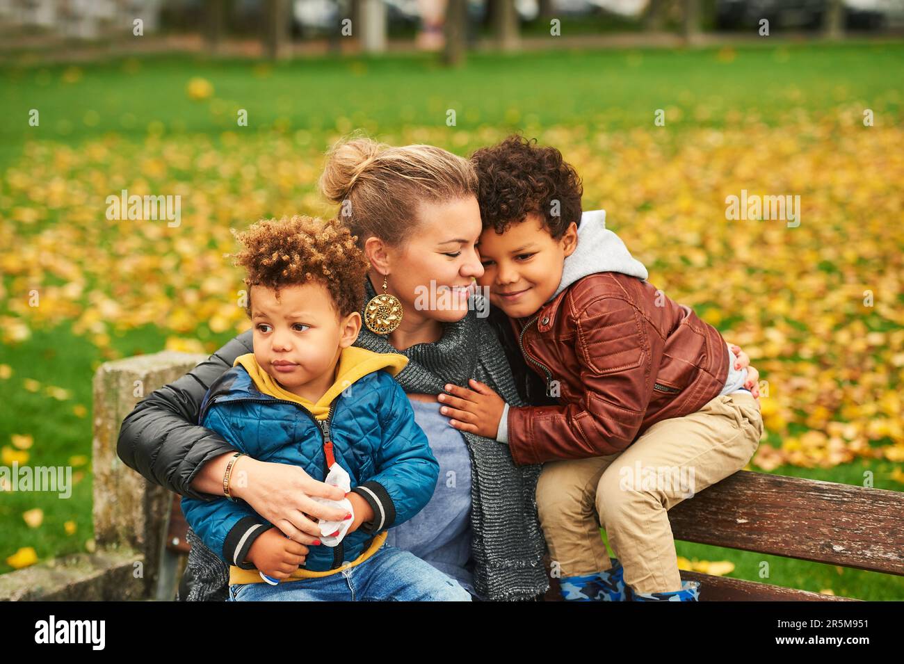 Portrait extérieur de la jeune mère heureuse avec deux fils charmants, famille appréciant la belle journée d'automne dans le parc public, famille de race mixte Banque D'Images