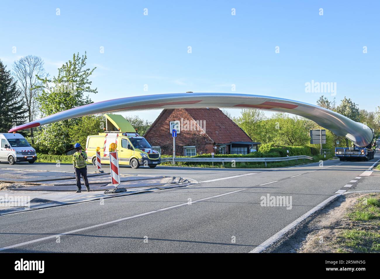 Transport intensif d'une lame de moulin à vent sur une jonction étroite de la route de campagne avec des obstacles comme des maisons et des arbres, industrie de centrale électrique pour les énergies renouvelables fr Banque D'Images