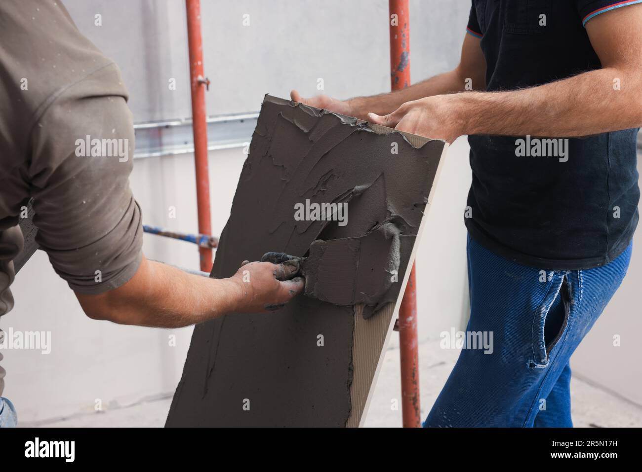 L'employé répandant le mélange d'adhésif sur les carreaux avec une spatule, gros plan Banque D'Images
