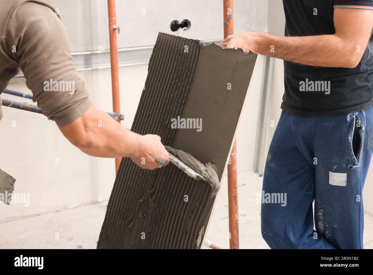 L'employé répandant le mélange d'adhésif sur les carreaux avec une spatule, gros plan Banque D'Images