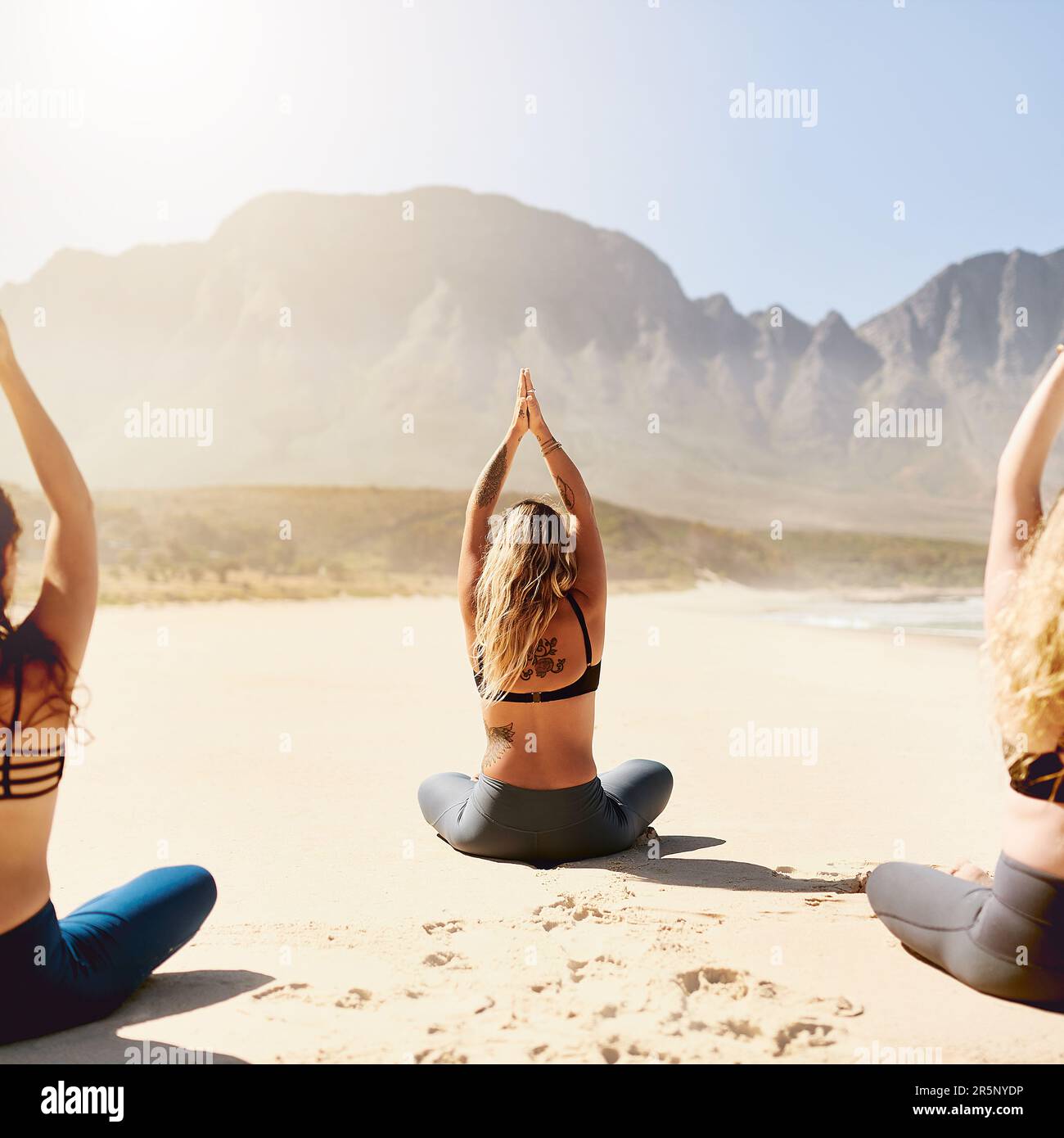 Le yoga vous aide à devenir plus léger, plus sain et plus heureux. Vue arrière de trois jeunes femmes pratiquant le yoga sur la plage. Banque D'Images