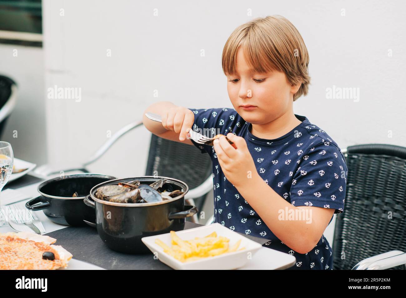 Enfant mangeant des moules cuites à la vapeur avec des frites dans le restaurant en plein air Banque D'Images