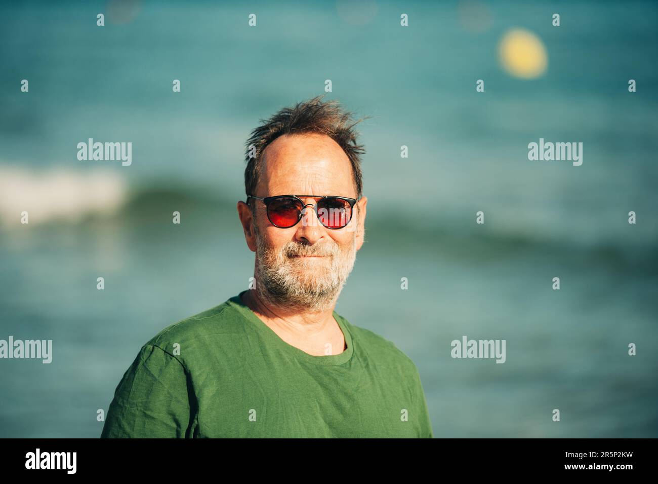 Portrait extérieur de l'homme heureux d'âge moyen profitant d'une belle journée ensoleillée sur la plage, portant un t-shirt vert et des lunettes de soleil Banque D'Images