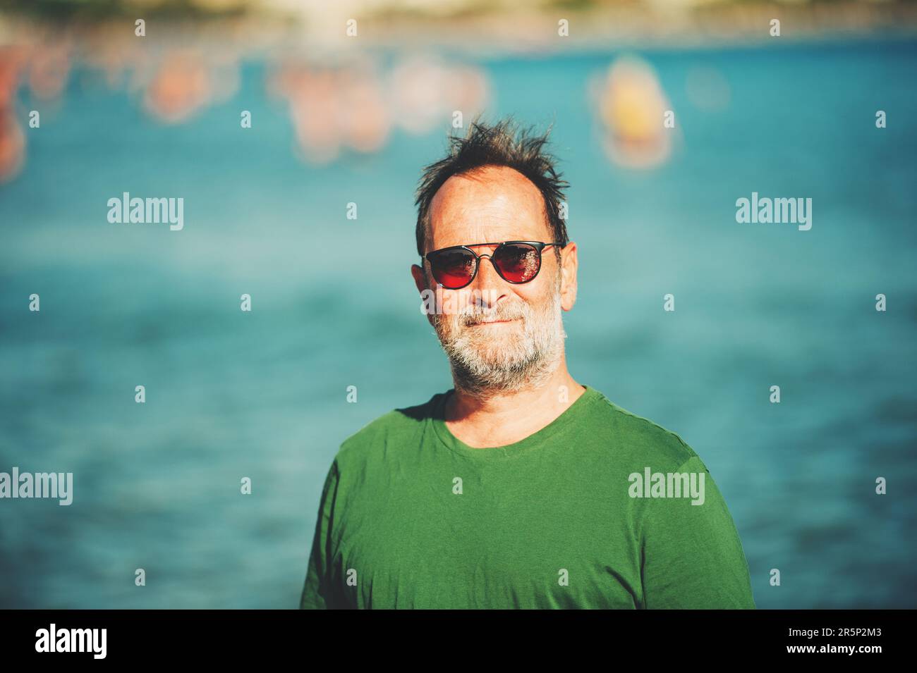 Portrait extérieur de l'homme heureux d'âge moyen profitant d'une belle journée ensoleillée sur la plage, portant un t-shirt vert et des lunettes de soleil Banque D'Images