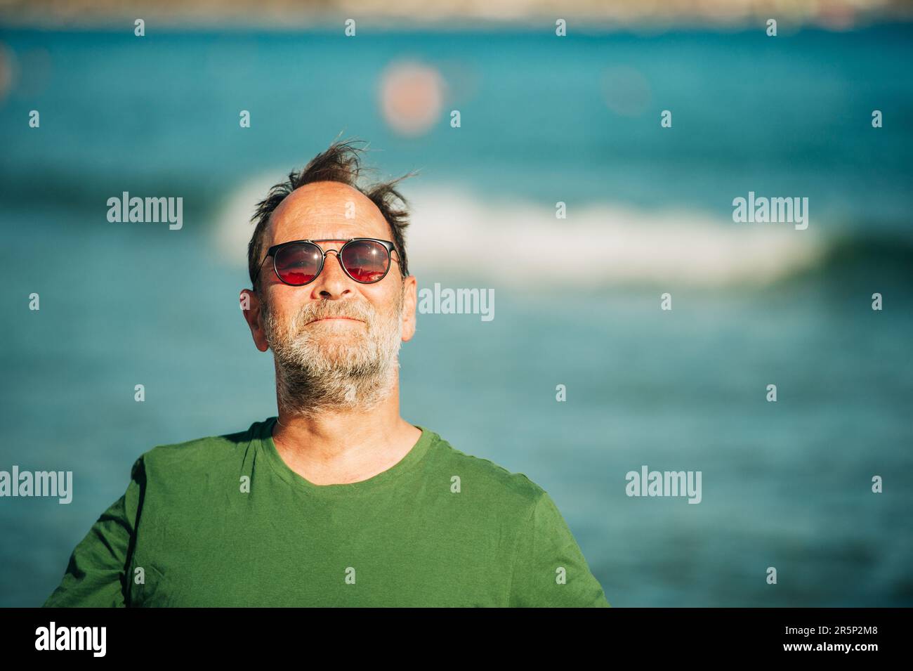 Portrait extérieur de l'homme heureux d'âge moyen profitant d'une belle journée ensoleillée sur la plage, portant un t-shirt vert et des lunettes de soleil Banque D'Images