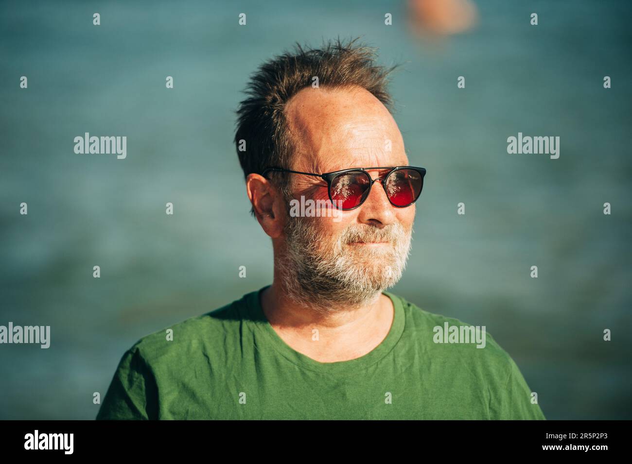 Portrait extérieur de l'homme heureux d'âge moyen profitant d'une belle journée ensoleillée sur la plage, portant un t-shirt vert et des lunettes de soleil Banque D'Images