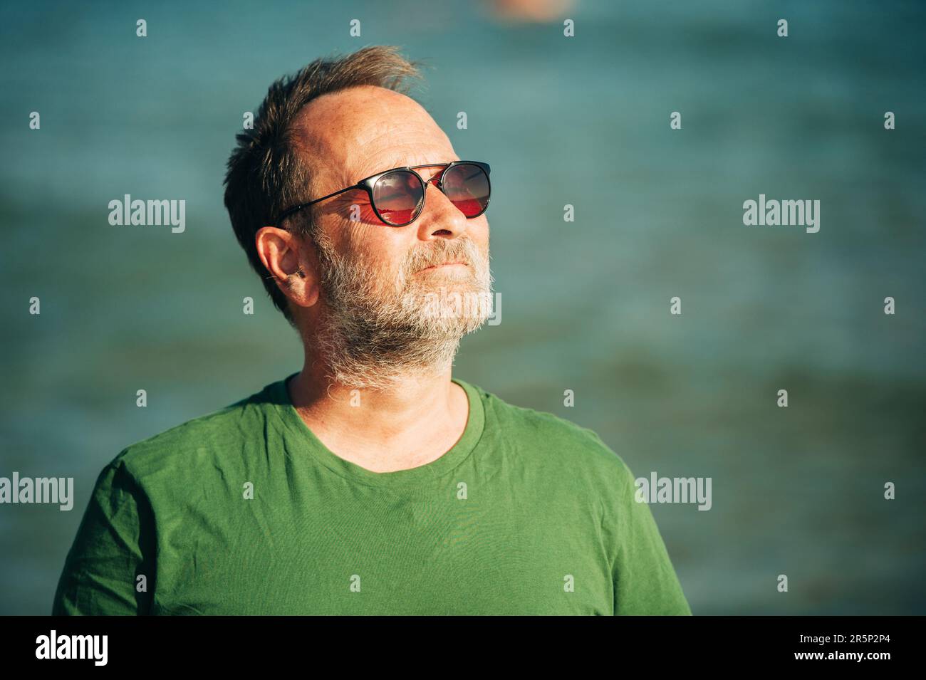 Portrait extérieur de l'homme heureux d'âge moyen profitant d'une belle journée ensoleillée sur la plage, portant un t-shirt vert et des lunettes de soleil Banque D'Images