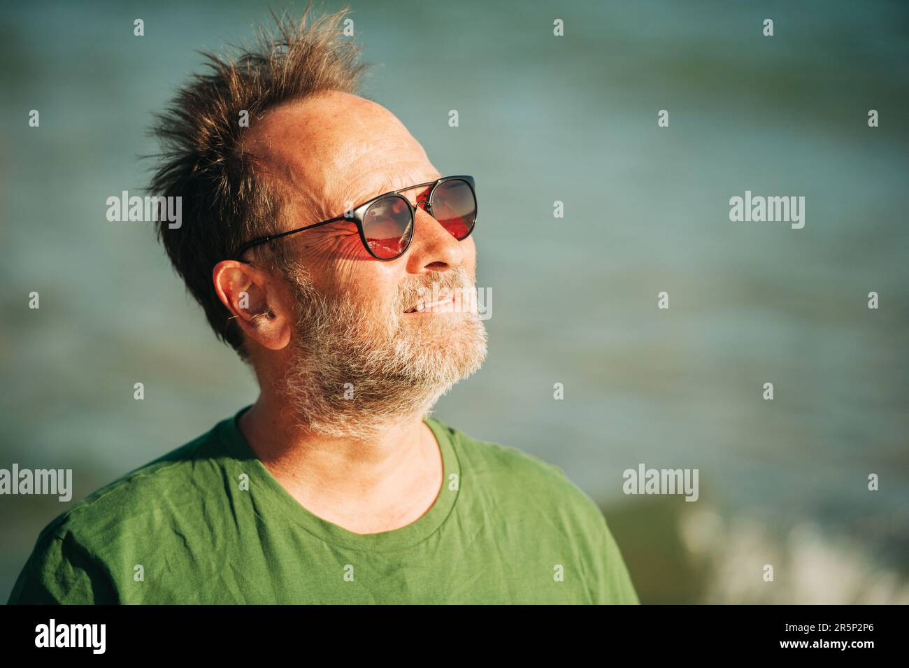 Portrait extérieur de l'homme heureux d'âge moyen profitant d'une belle journée ensoleillée sur la plage, portant un t-shirt vert et des lunettes de soleil Banque D'Images