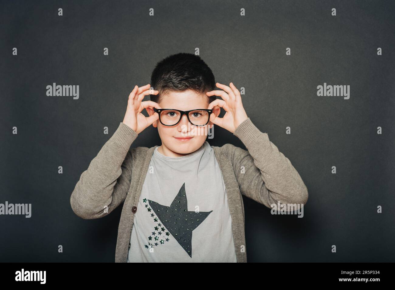 Studio portrait de jeune garçon beau posant sur fond noir, portant des lunettes Banque D'Images