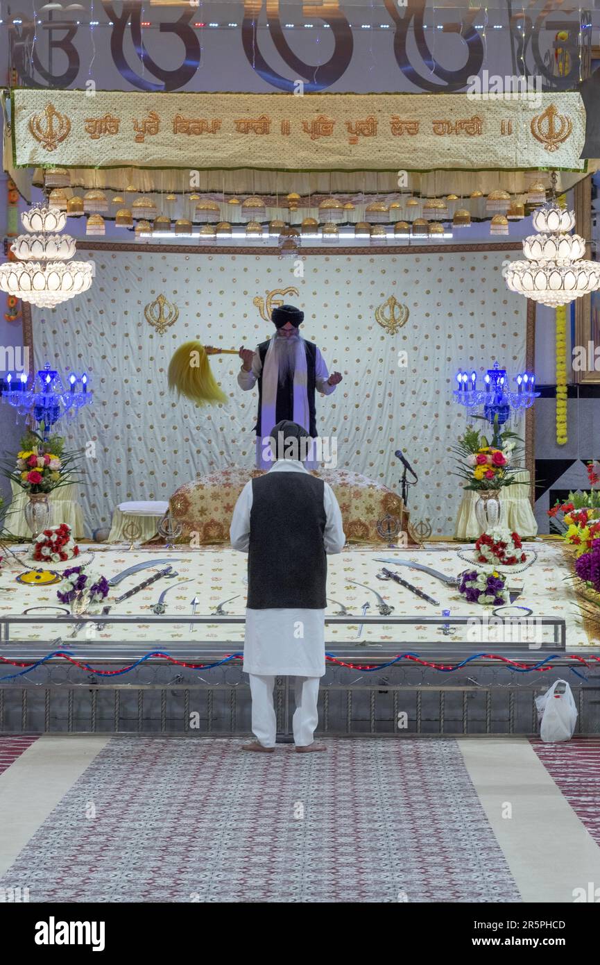 Un pries sikh (premier plan) dirige un service tandis qu'un second prêtre fait passer son flan jaune cérémonial sur la bible sikh. Dans un temple de Queens, New York Banque D'Images