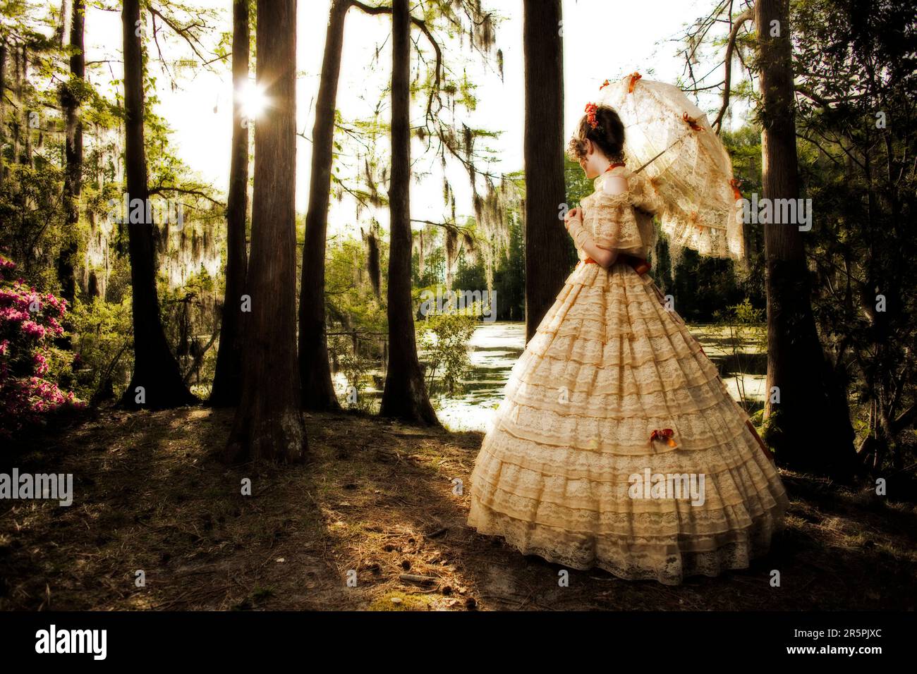 Une jeune femme pose dans une tenue Belle du Sud , comprenant une grande robe d'époque ornée et un parasol, près d'un lac. Banque D'Images