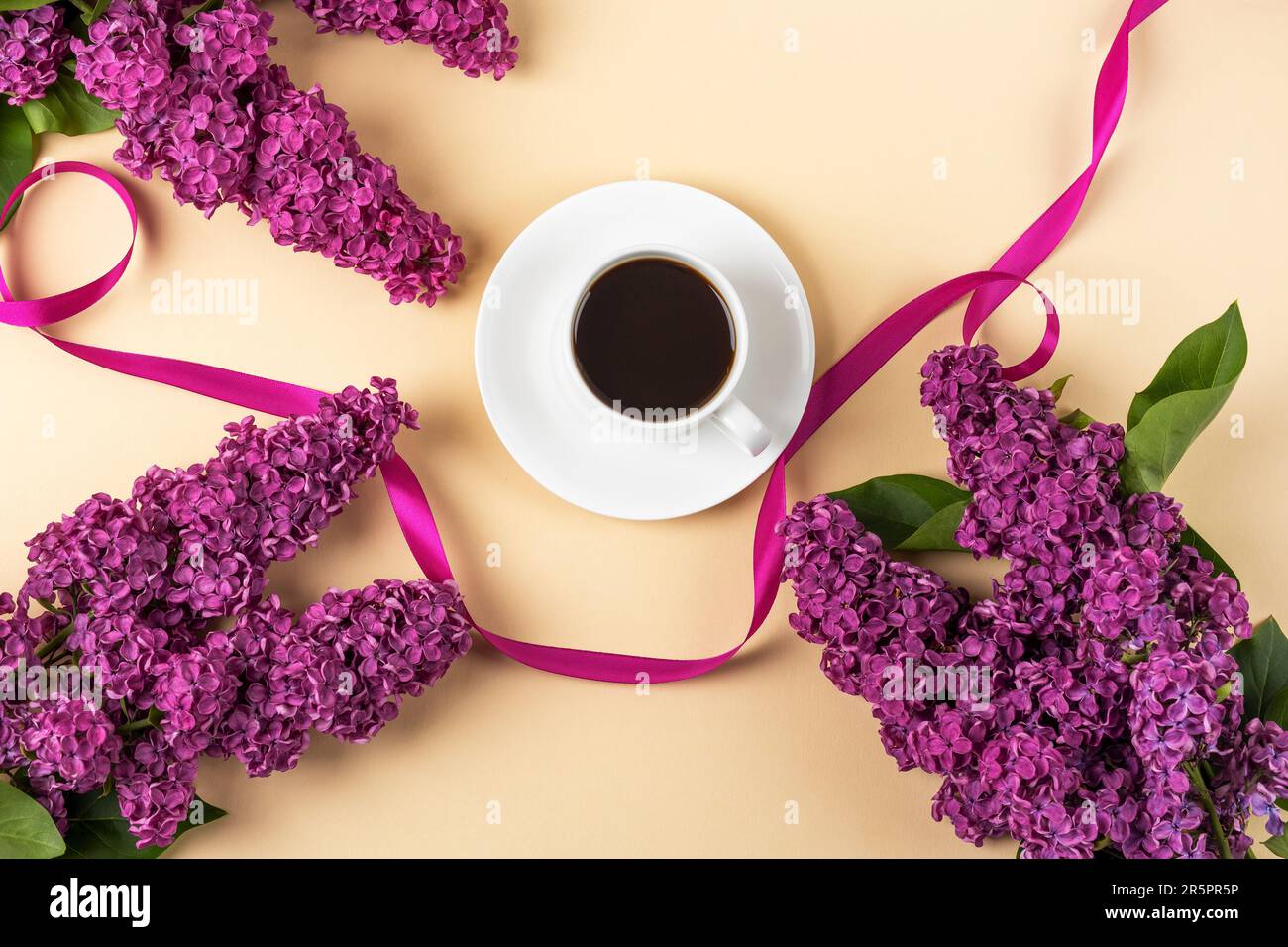 Tasse de café noir frais et branche de lilas violets fleuris avec ruban de satin sur fond orange. Pause café. Fleurs de printemps. Plan d'agencement, vue de dessus Banque D'Images