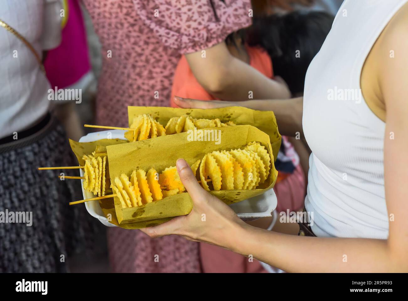 Mains tenant une boîte de papier avec frites de pommes de terre sur brochettes dans le marché nocturne vietnamien Banque D'Images